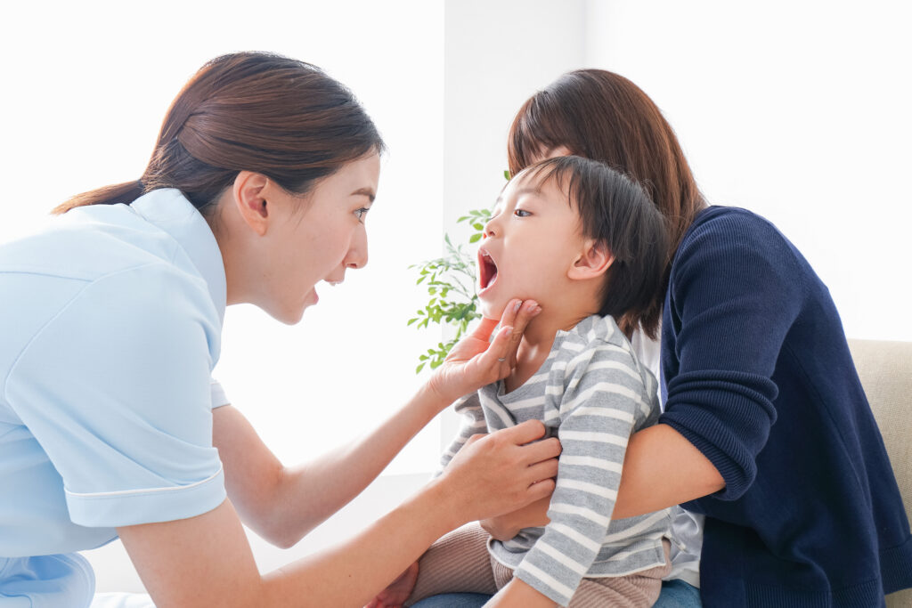 母親の膝の上に乗った子供が医師に口の中を見られている